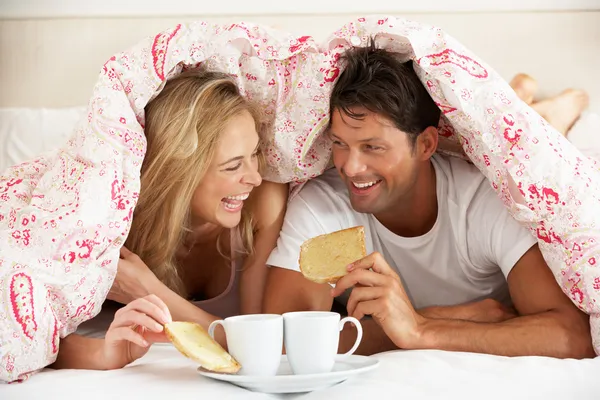 Пара прижалась под пищевым завтраком пухового одеяла — стоковое фото