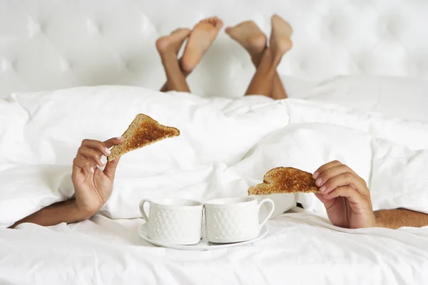 Пара, скрывающаяся под завтраком наслаждения пухового одеяла в постели — стоковое фото