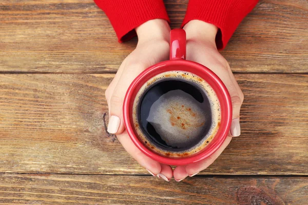 Женские руки, держа чашку кофе на деревянных фоне — стоковое фото