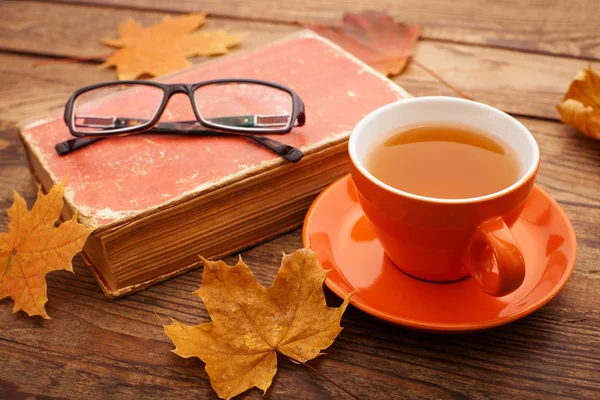 Осенние листья, книга и чашка чая на деревянном столе в студии — стоковое фото