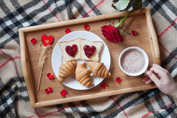 Романтический завтрак в постели с розовым цветком и лепестками. Тосты в форме сердца джем, круассаны, кофе на деревянный поднос — стоковое фото