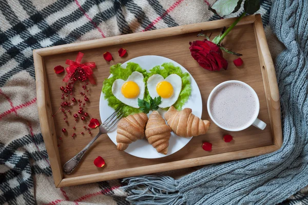 Вкусный романтический завтрак в постели сюрприз форме сердца яйца, варенье тосты, круассаны, розы и лепестки на деревянный стол лотка. Концепция здорового питания День Святого Валентина — стоковое фото